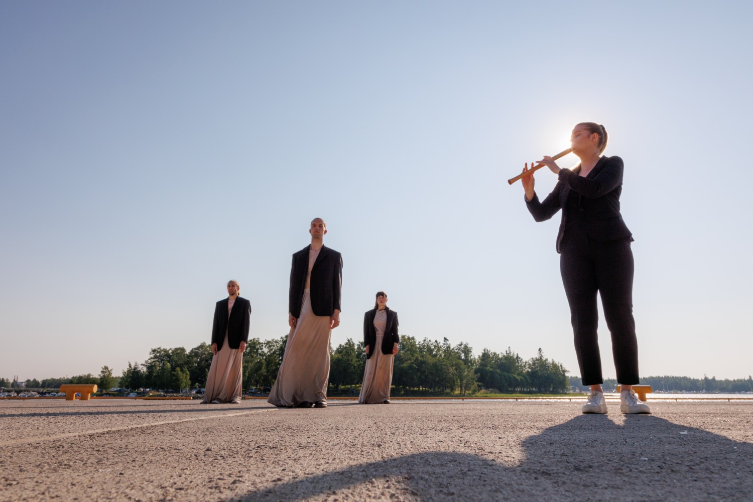 A woman playing a flute and three dancers standing behind in dresses