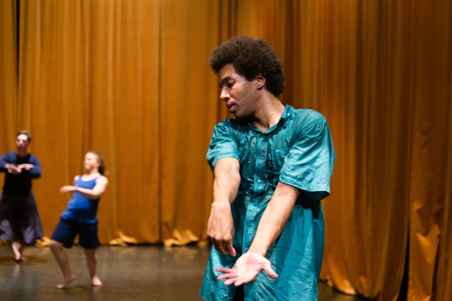 A man dancing in a turquoise shirt in front of an orange curtain