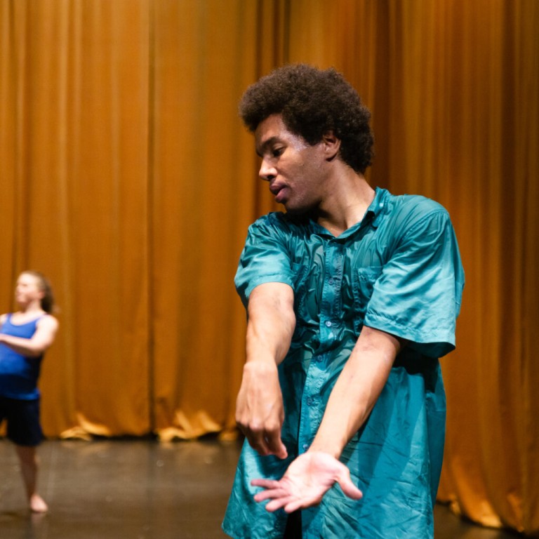 A man dancing in a turquoise shirt in front of an orange curtain
