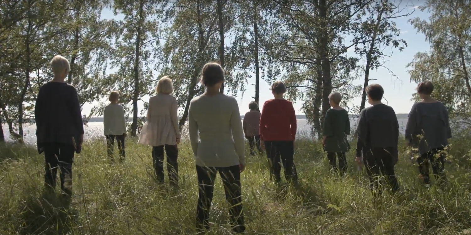A group of people stand in a forest facing back