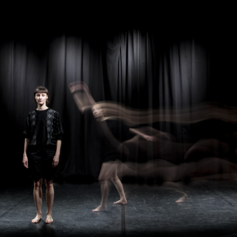 A woman stands on a black stage in black clotihng