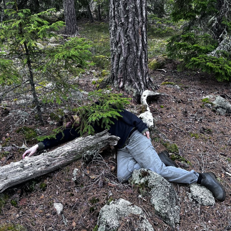 Henkilö makaa metsässä kaantuneen puun vieressä
