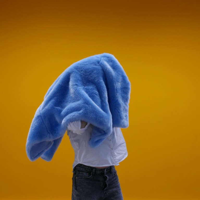 A woman holds a blue fur coat on her head