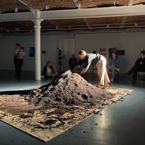 A woman touches a pile of dirt in a gallery space